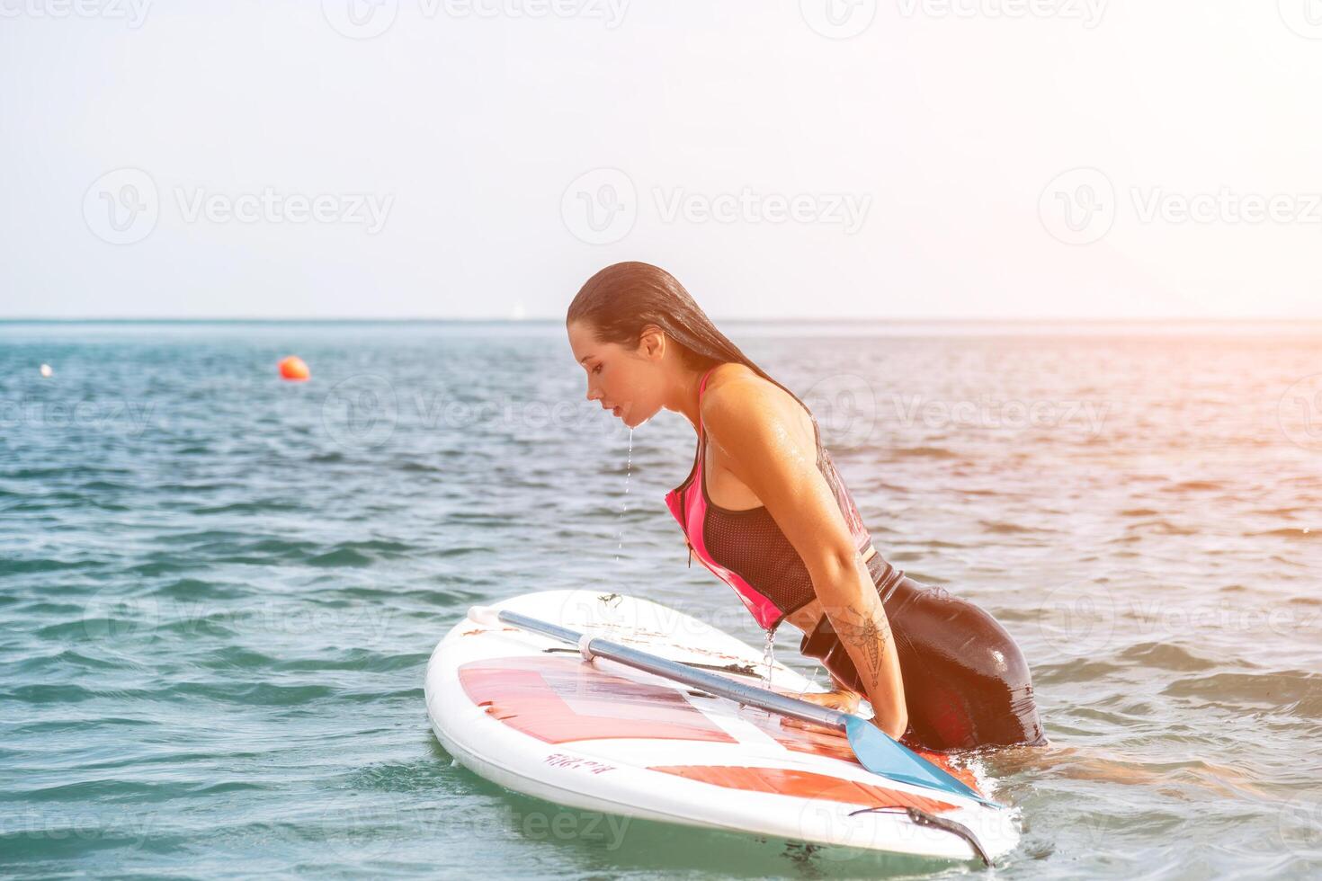 Sea woman sup. Silhouette of happy young woman in pink bikini, surfing on SUP board, confident paddling through water surface. Idyllic sunset. Active lifestyle at sea or river photo