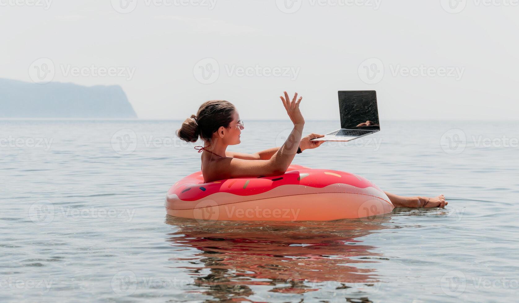 Woman Laptop Beach - Working remotely on vacation while floating on an inflatable ring in the ocean. photo