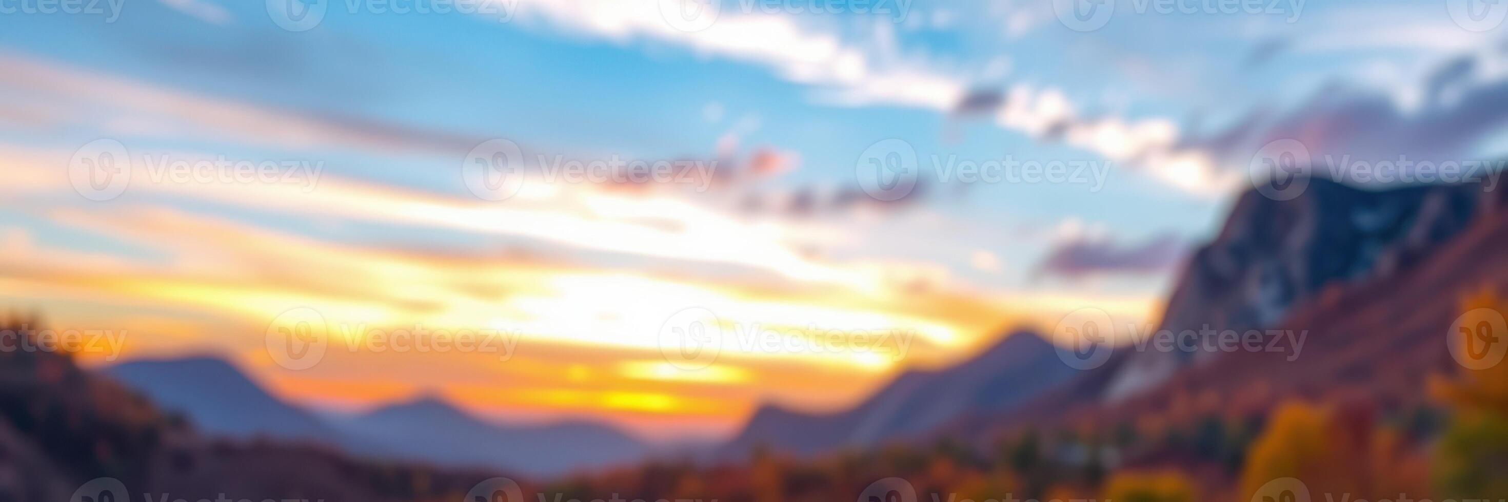 Vibrant sunset casts warm hues over mountain landscape with clouds and silhouettes of peaks in the distance photo