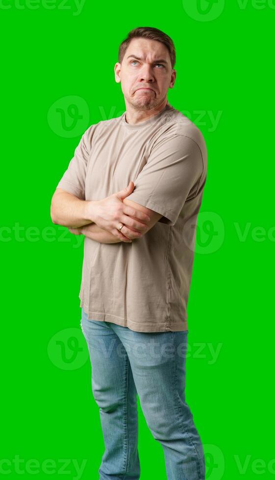 A man stands with arms crossed and a thoughtful expression in front of a green screen photo