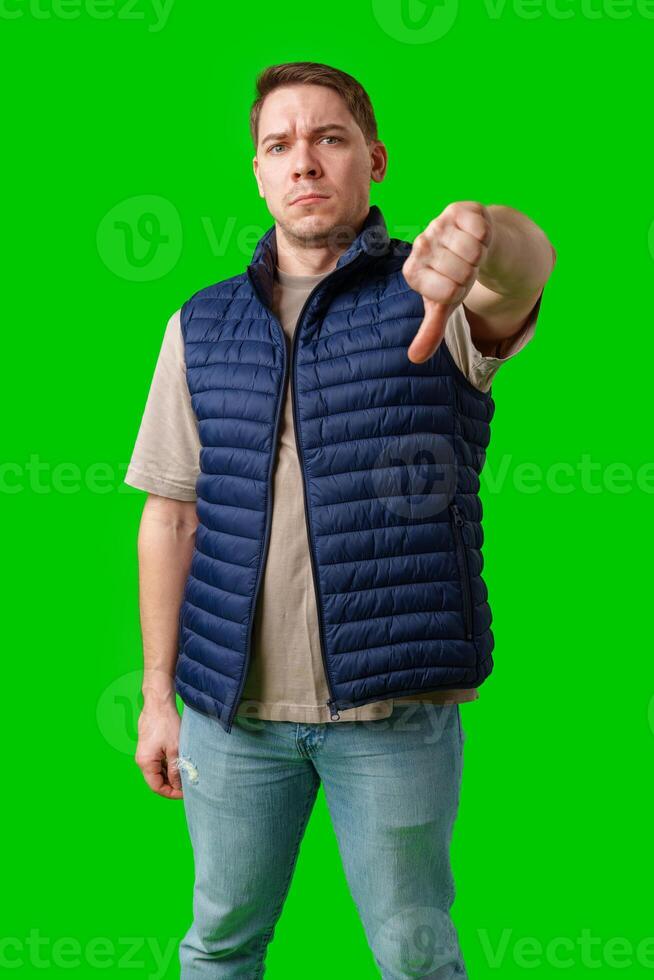 Man in a blue vest showing a thumbs down gesture with a bright green background photo