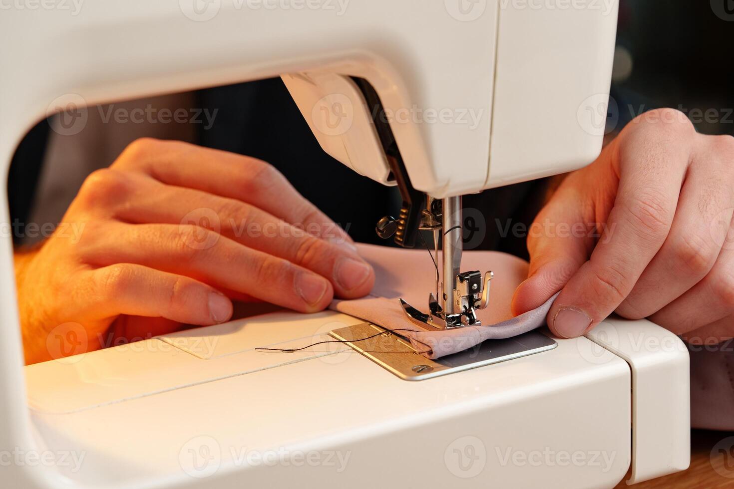 Hands sewing fabric using a sewing machine on a wooden table in a well-lit workspace photo