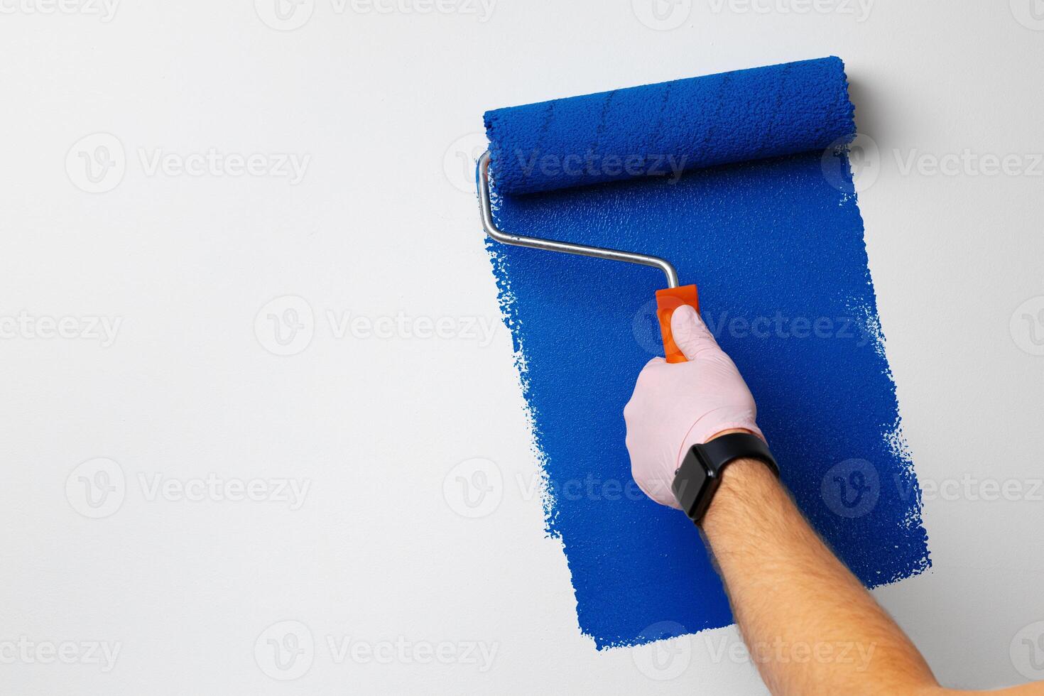 Gloved male hand painting wall into classic blue color photo