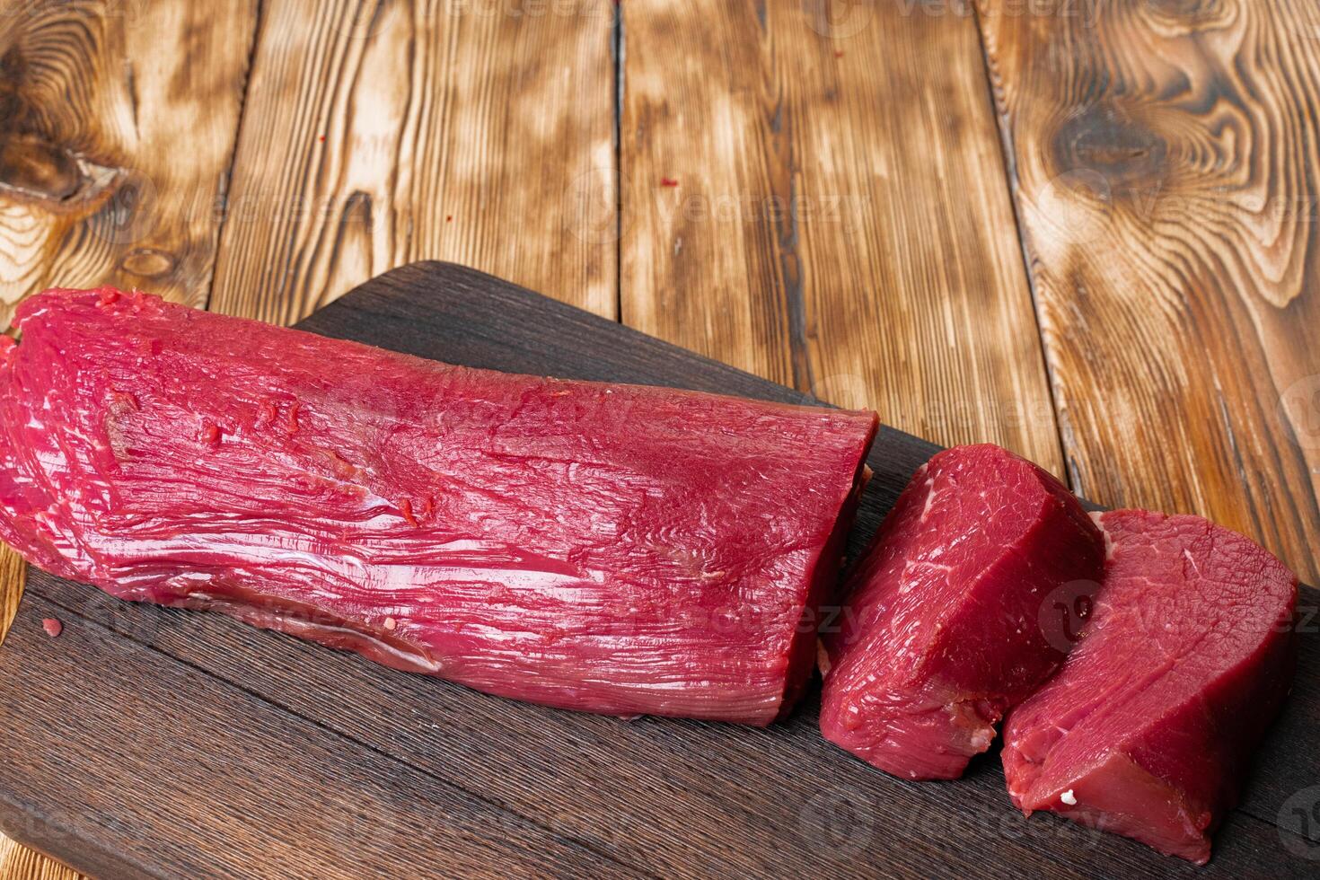Slices raw meat fillet on wooden board photo