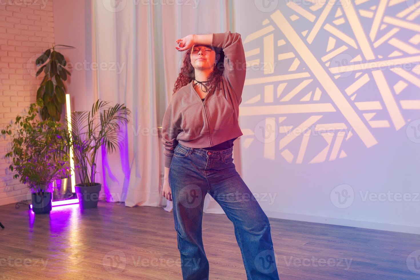 A woman poses in front of a wall with a geometric light projection, in a studio setting photo