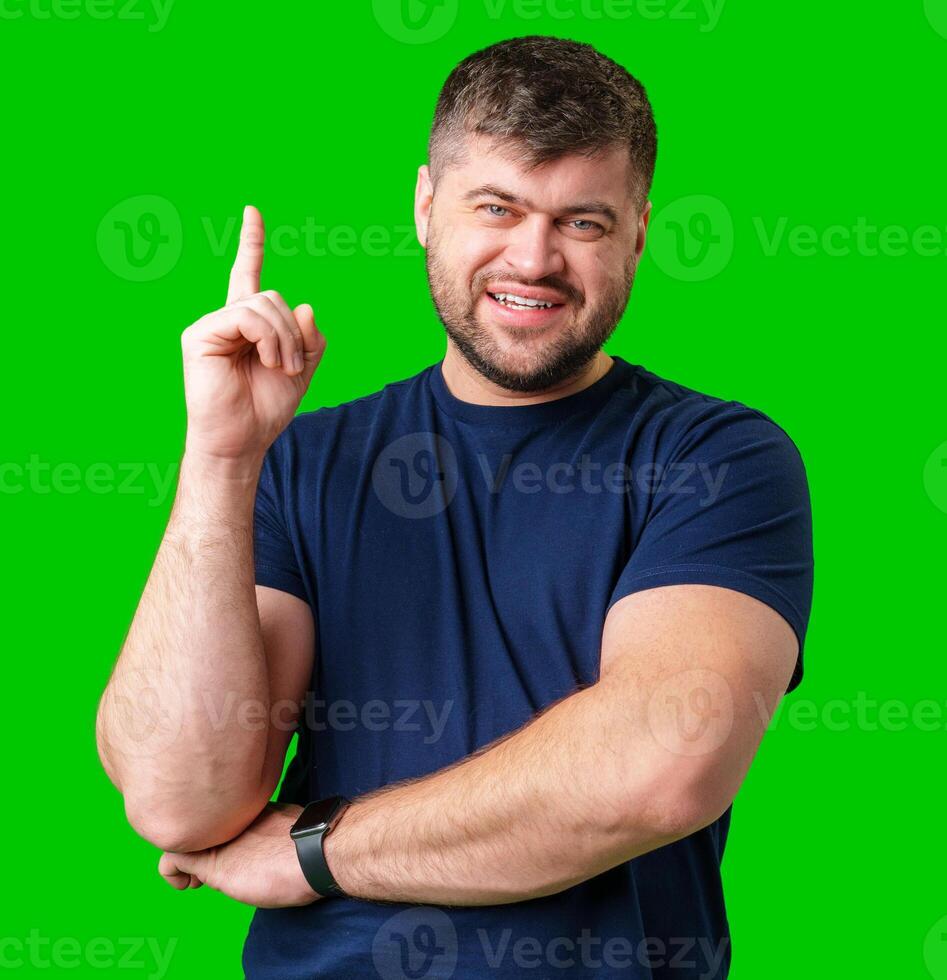 A man with a friendly smile gestures upwards while wearing a navy shirt against a bright green background photo