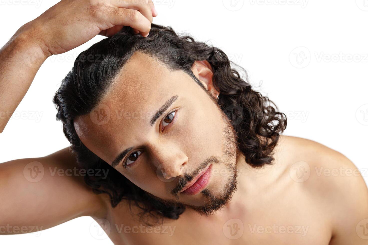 Young man with curly hair thoughtfully posing against a plain background photo