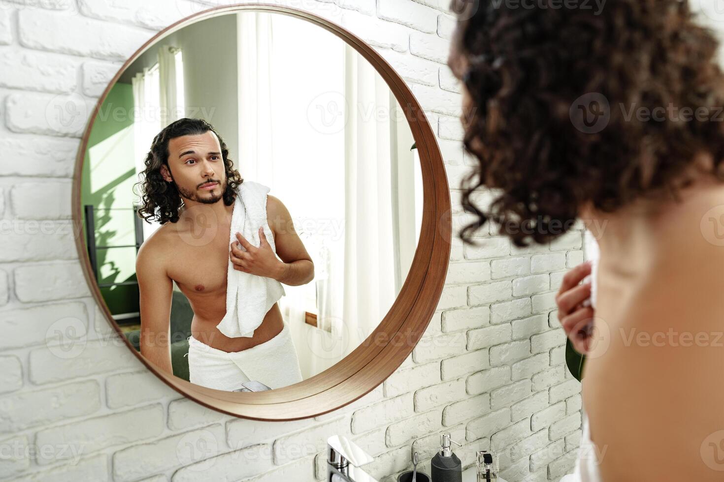Young man grooming himself in a modern bathroom mirror with natural lighting photo