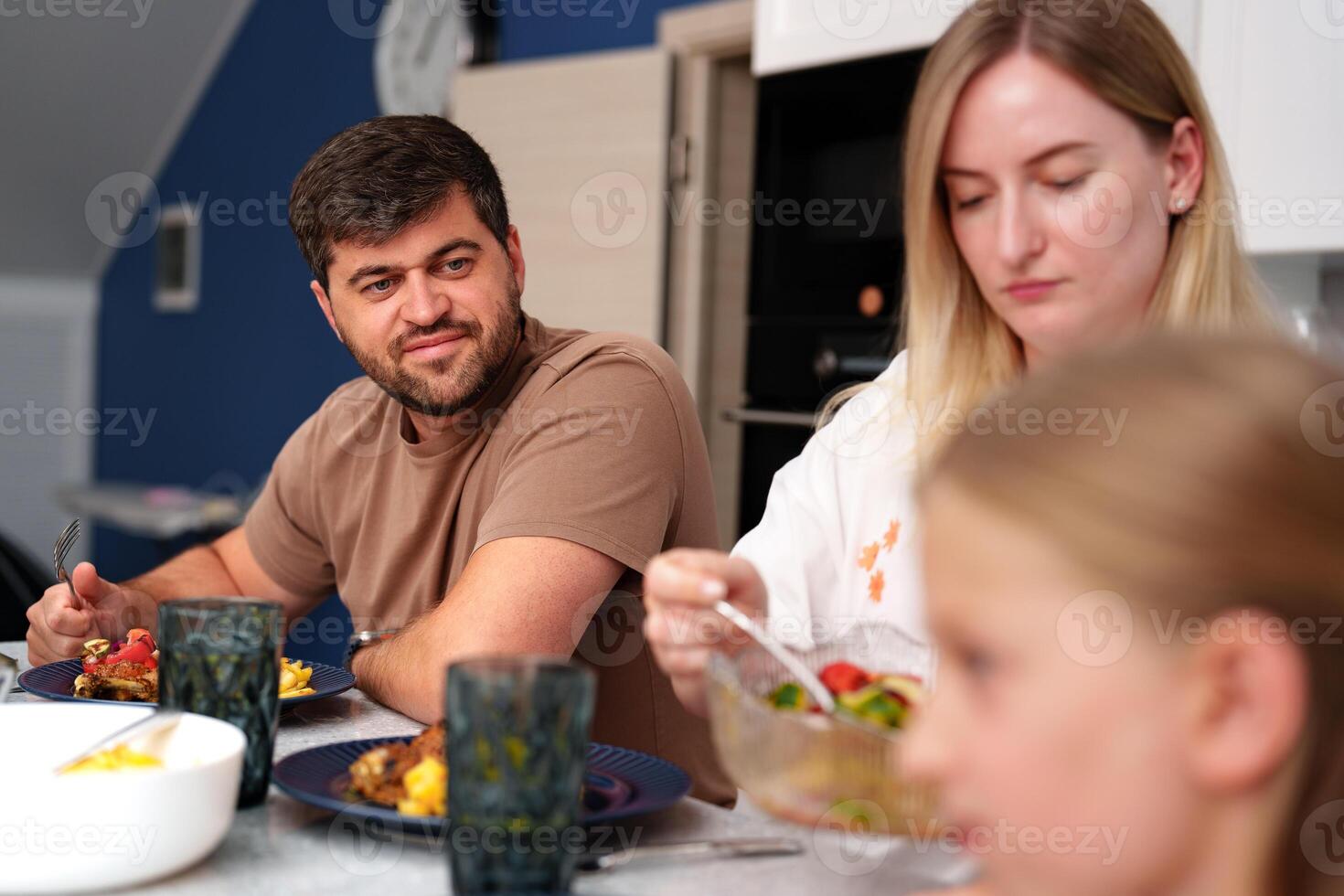 A man and a woman sit at a kitchen table eating lunch while a young child sits beside them photo