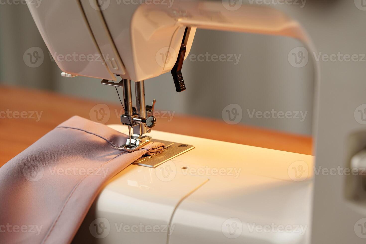 Sewing machine in use on a wooden table, stitching a light fabric in a well-lit indoor workspace photo