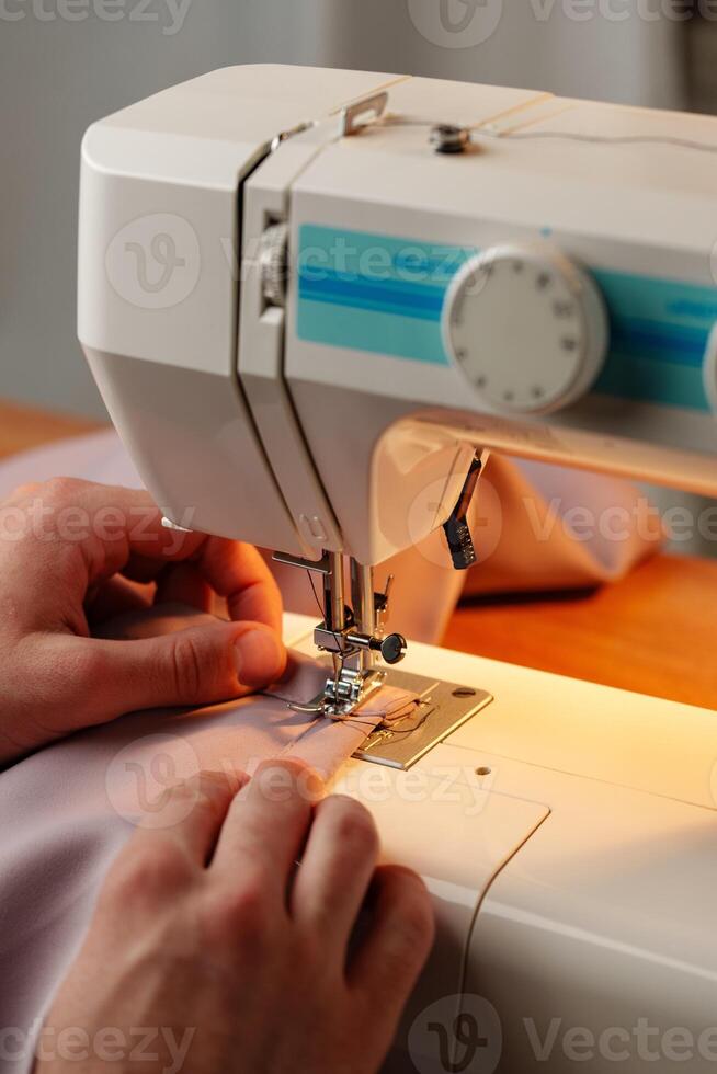 Hands sewing fabric using a sewing machine on a wooden table in a well-lit workspace photo