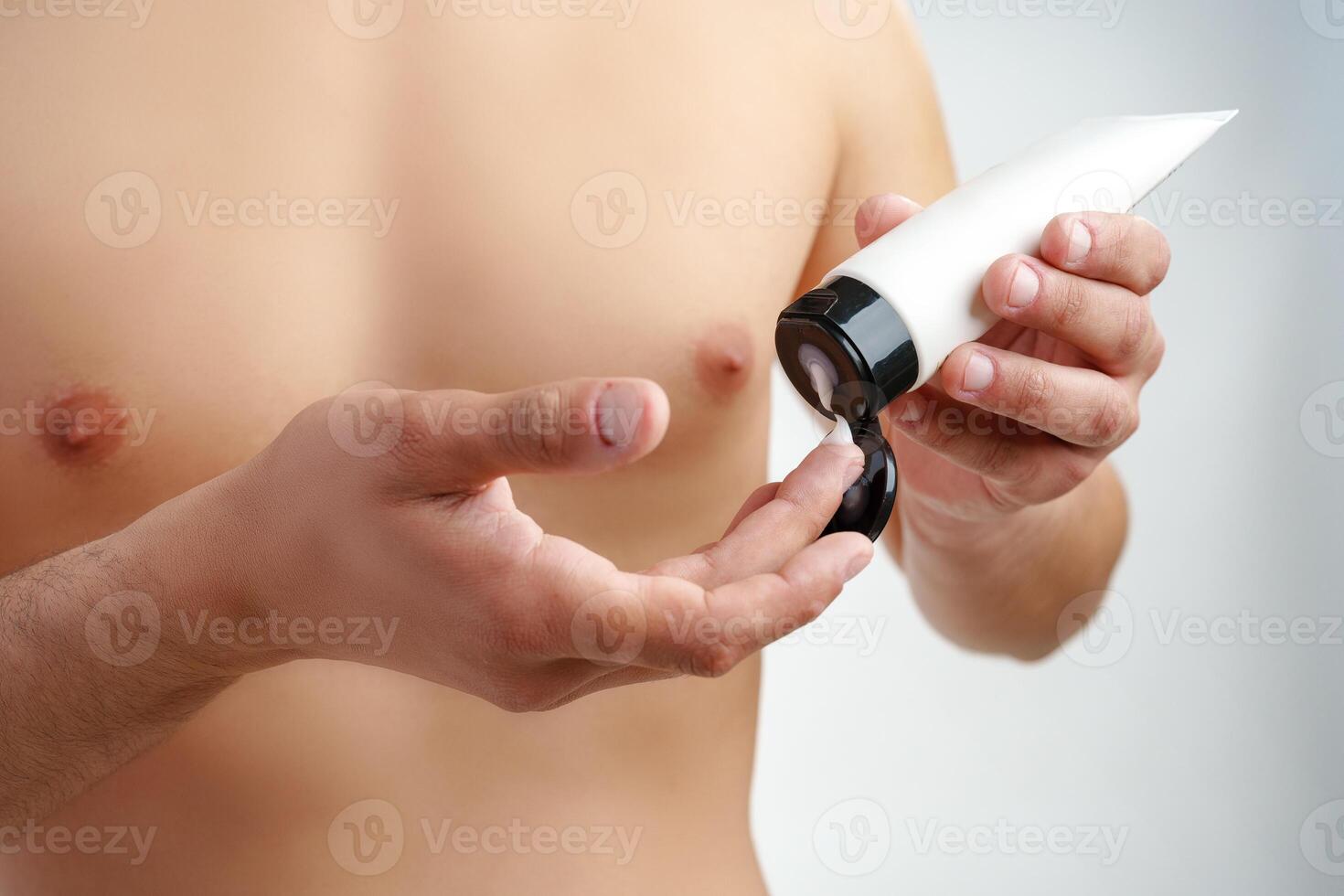 A young man applying skincare cream on his face with a focused expression, demonstrating personal grooming at home photo