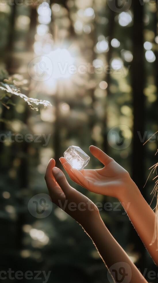 Hands holding a crystal object in sunlight filtering through trees in a forest photo