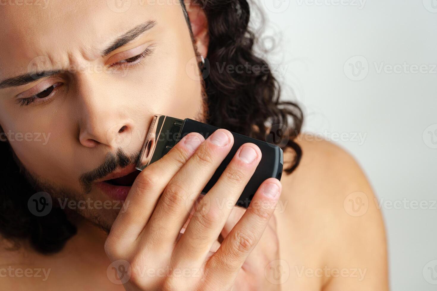 Man trimming his beard indoors using an electric trimmer while showcasing his personal grooming routine photo