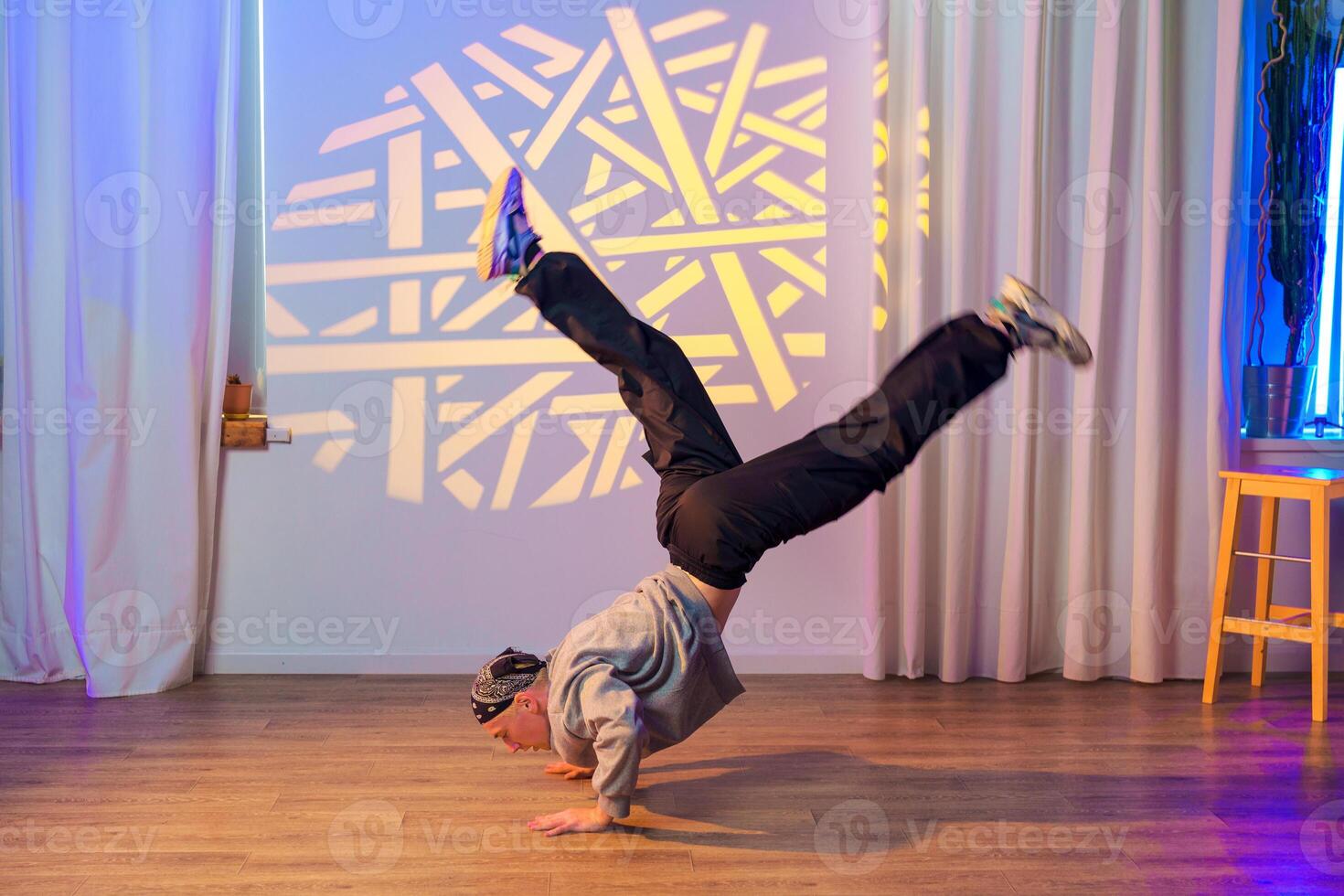 A dancer performs a dynamic move in a studio with a geometric light projection behind him photo