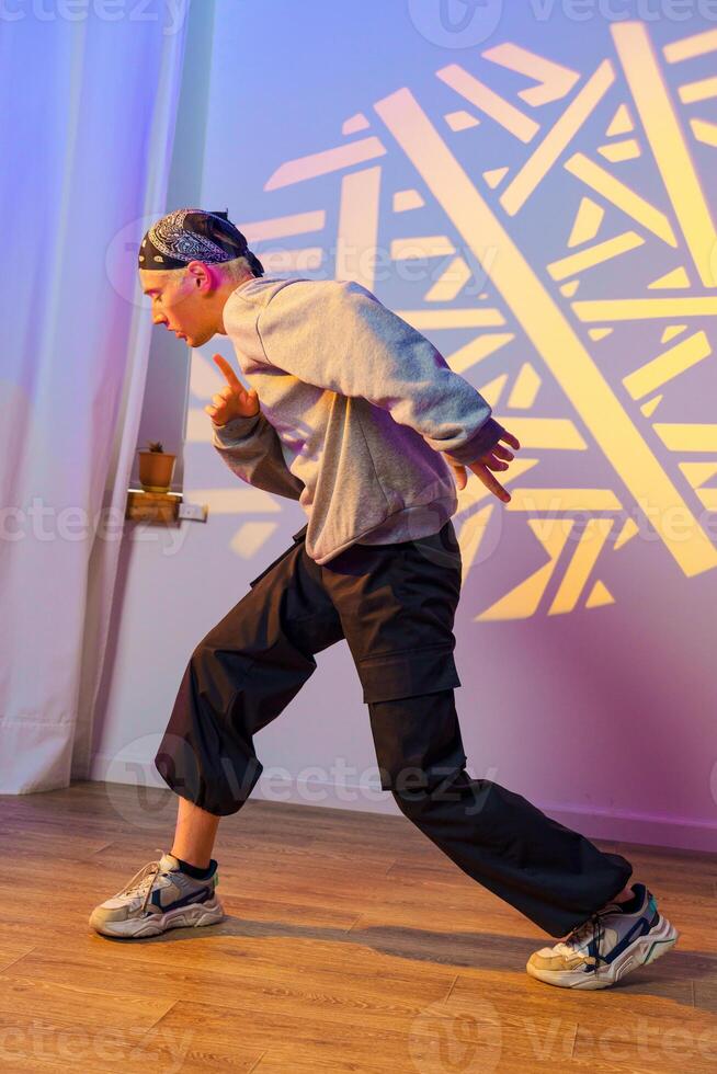 A young man dances in a studio with a geometric light projection on the wall photo