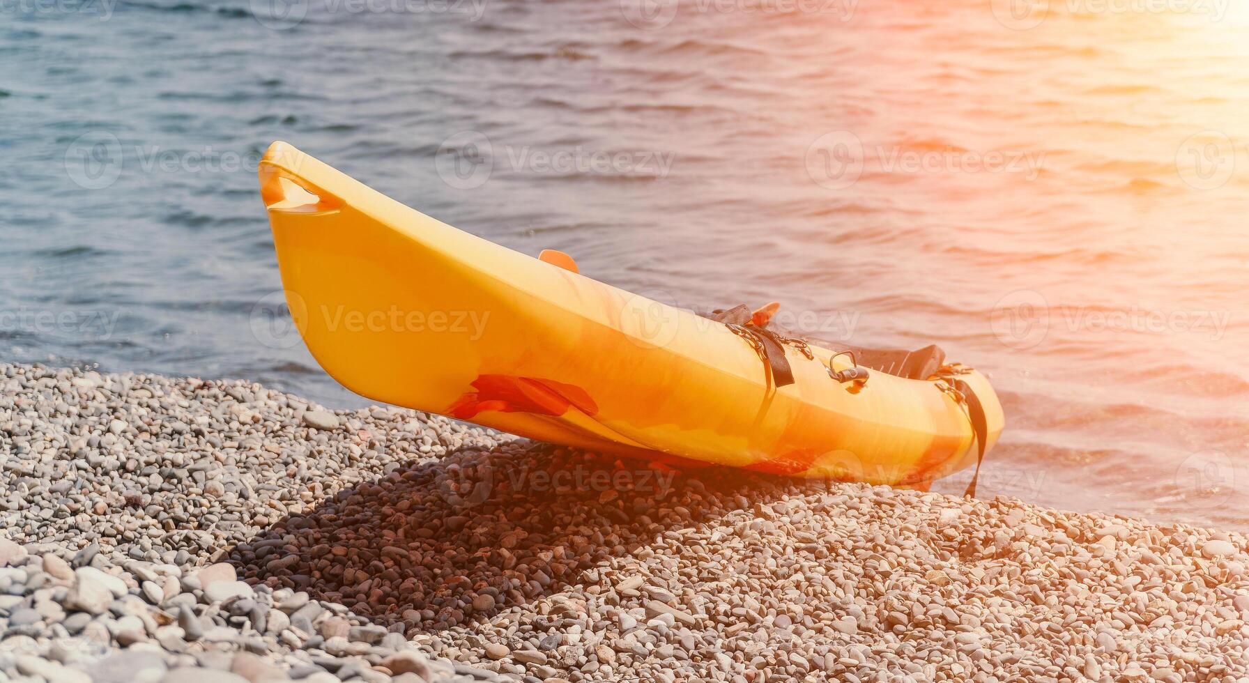 Kayak Beach Summer - Yellow kayak on a pebble beach with sunlight in the background. photo