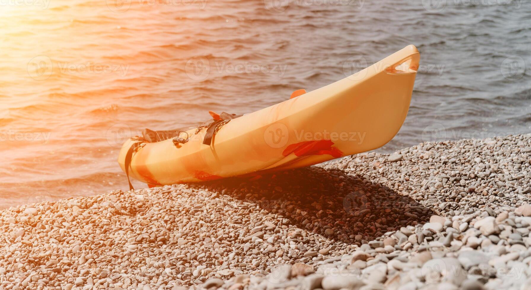 Kayak Beach Water - A yellow kayak rests on a pebbled beach with the sun reflecting off the water. photo