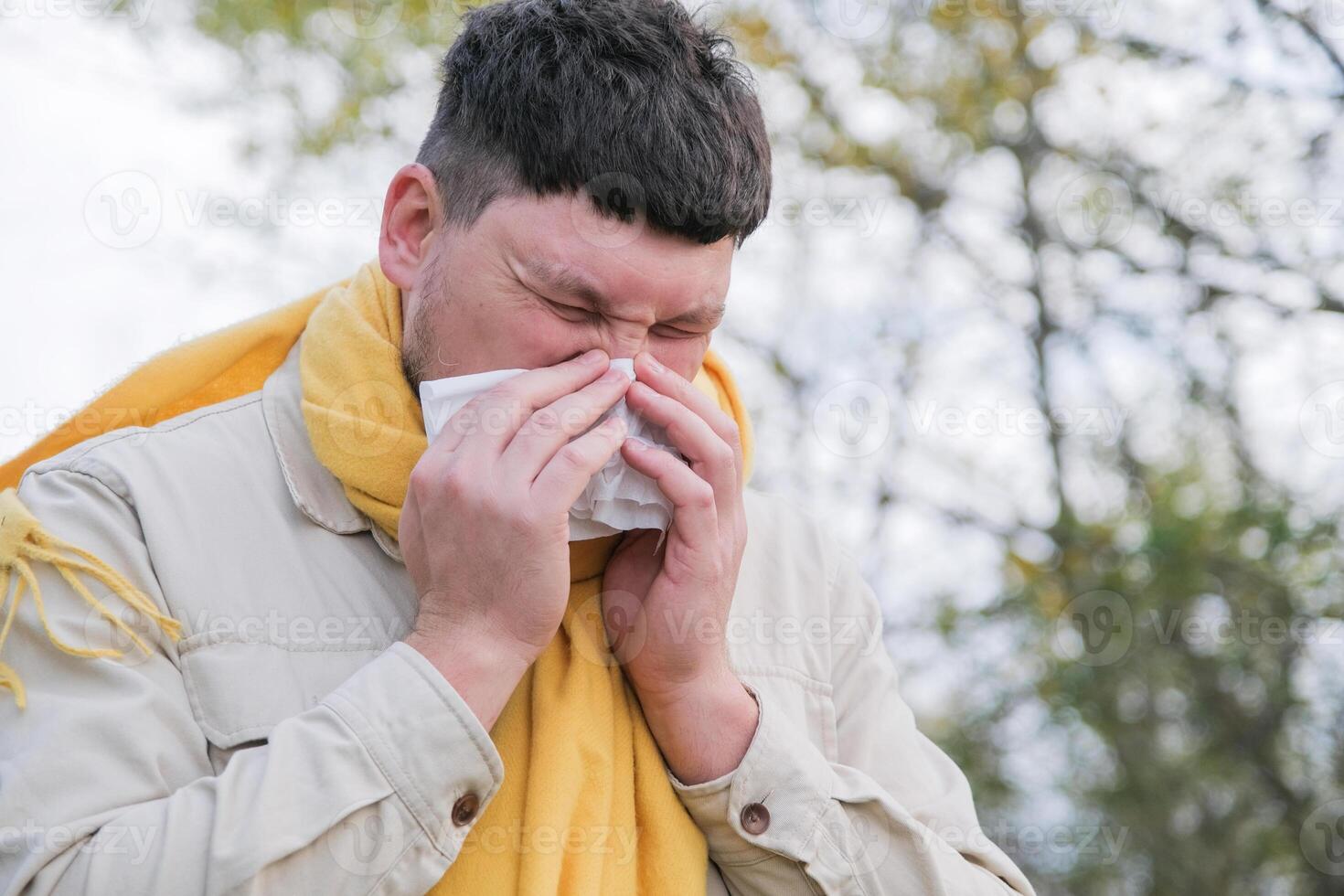 young man enjoying autumn days breathing fresh air using tissue to wipe nose photo