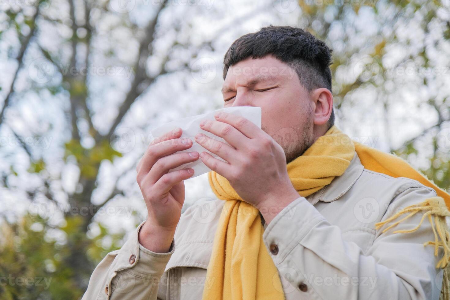 young man enjoying autumn days breathing fresh air using tissue to wipe nose photo