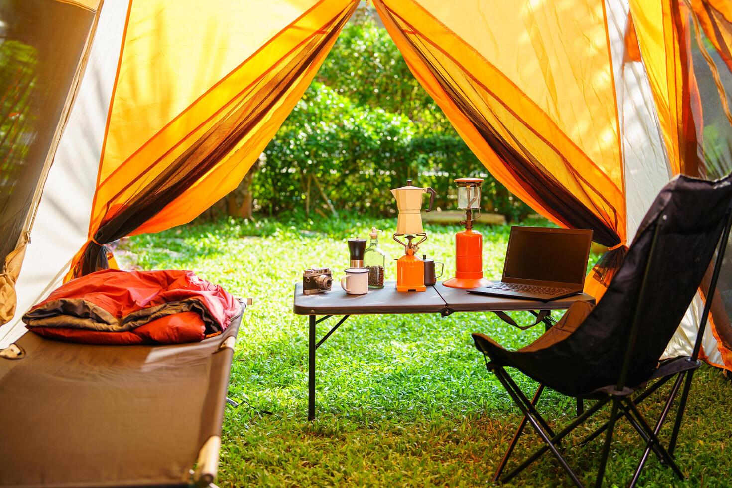 The folding bed inside the tent in the morning, gas lantern and coffee sets, notebooks on a wooden camping table, and outdoor ideas. photo