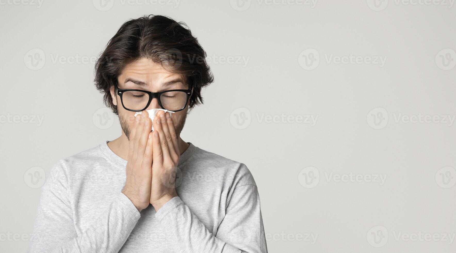 Runny nose and allergy concept. Guy in glasses wipes nose with napkins photo