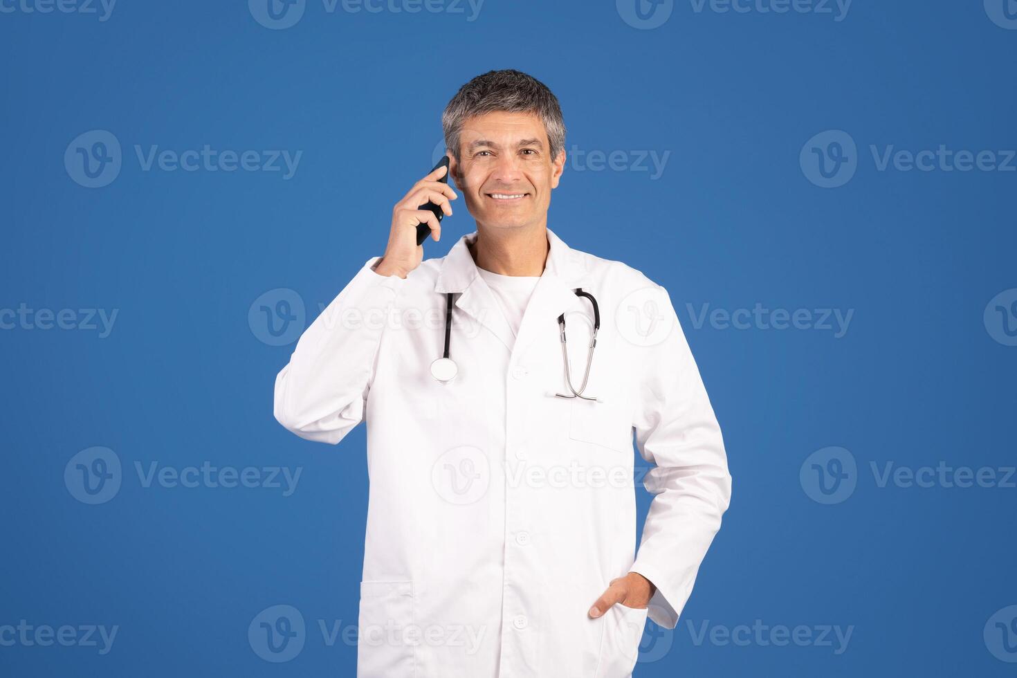 A middle aged Caucasian man in a white coat smiles while talking on his mobile phone. He exudes a confident and friendly demeanor in a clean, isolated background. photo