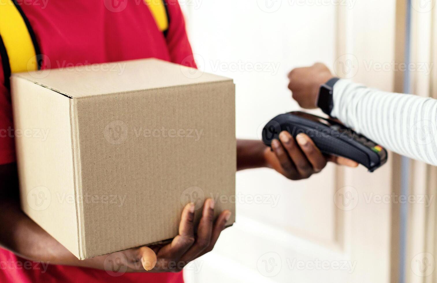 Cropped Shot Of Customer Lady Paying Courier For Parcel Delivery Using Smartwatch, Putting Watch To Payment Terminal At Home. Selective Focus On Cardboard Box photo