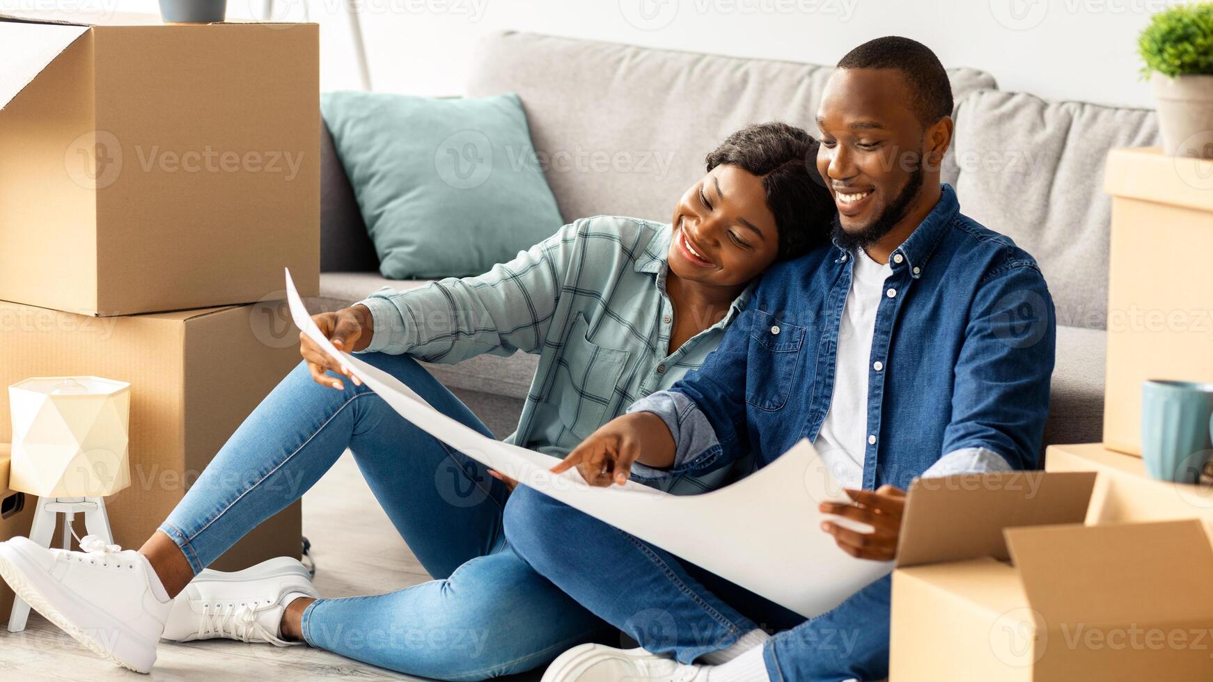 Black Spouses Planning Home Renovation, Checking Blueprints And Color Palette While Sitting Among Cardboard Boxes In Their New Apartment, African American Couple Decorating House After Moving photo