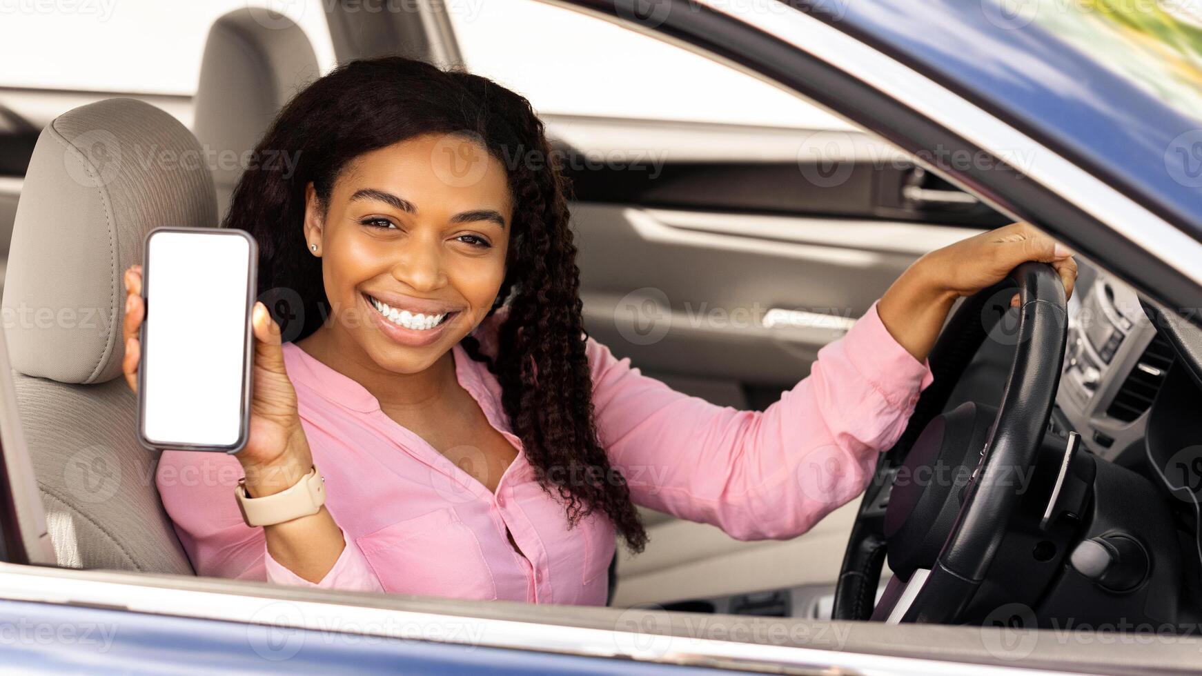 Happy black female driver holding smartphone with blank screen in hand, mock up, lady showing cell phone with white empty display, using mobile app for navigation, riding in city, free copy space photo