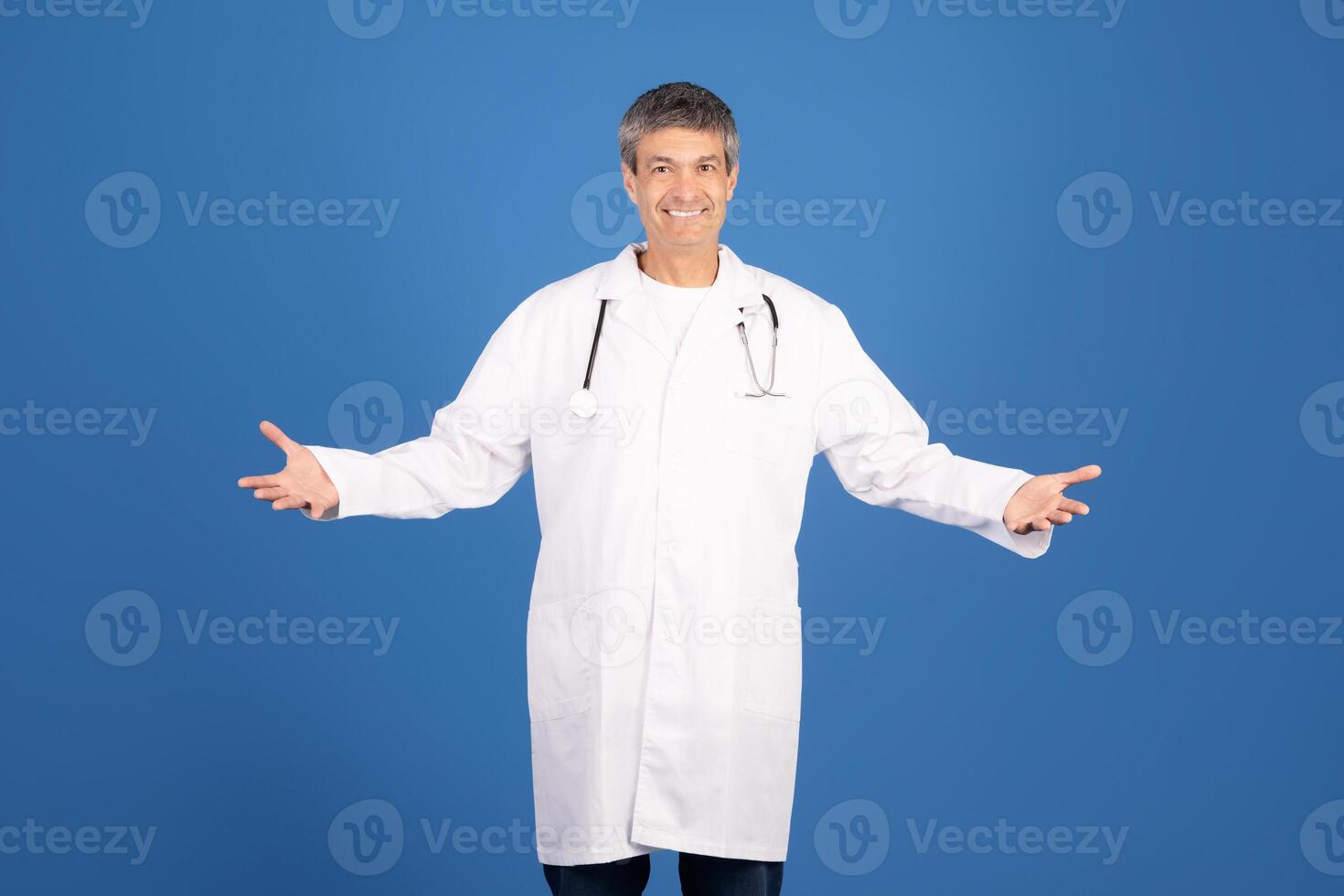 A mature Caucasian man in a white lab coat stands with open arms, smiling confidently. He represents a general physician, embodying the spirit of healthcare and professionalism. photo