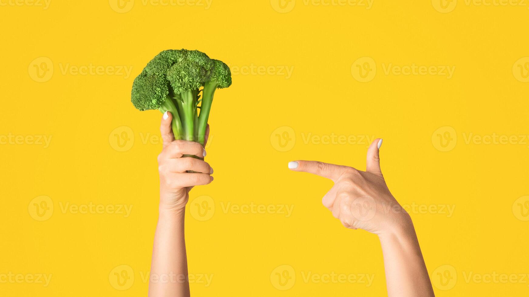 Woman pointing at broccoli in her hand against pink background, close up view. Panorama photo