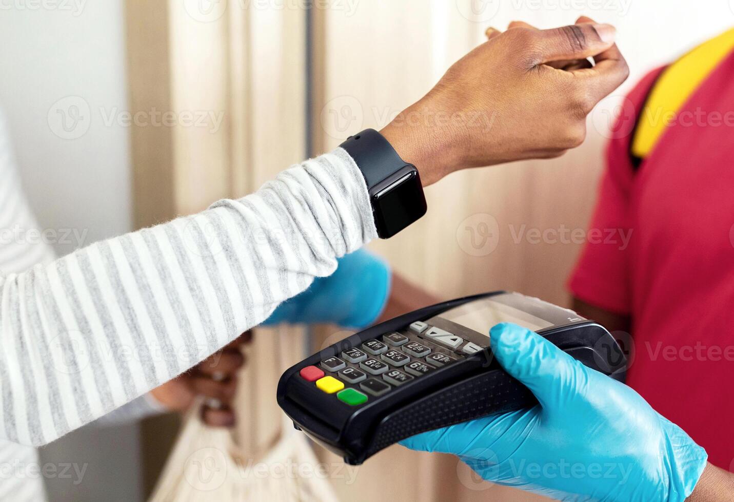 Grocery Delivery. African Female Paying Supermarket Courier Using Smartwatch For Payment Receiving Shopper Bag Full Of Groceries Products Standing Indoor. Cropped Shot, Selective Focus photo