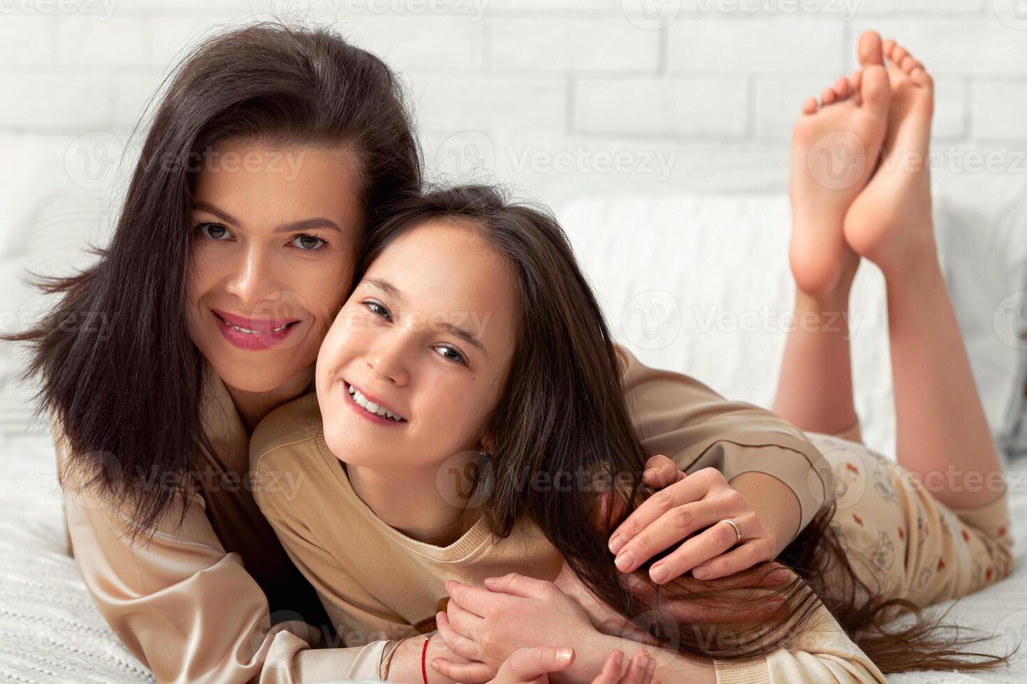 Teenage girl and her mother embracing on bed at home, giving each other hug, spending fun bonding times together. Mom and daughter friendship, family relationships concept photo