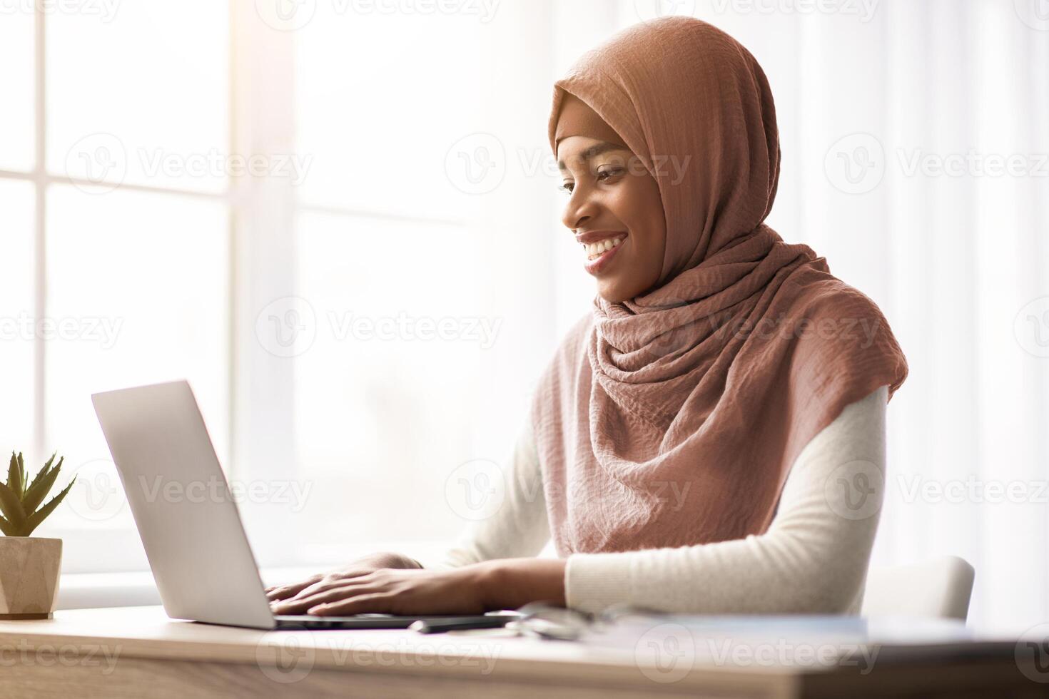Remote Work. Happy Black Muslim Freelancer Lady In Headscarf Using Laptop Computer, Cheerful African Islamic Woman In Hijab Sitting At Desk In Home Office And Typing On Keyboard, Free Space photo