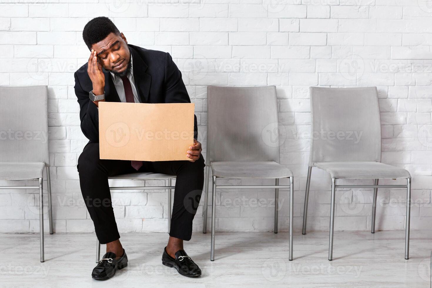 African American man in business suit holding sign LOOKING FOR JOB while waiting for interview in office lobby. Blank space photo