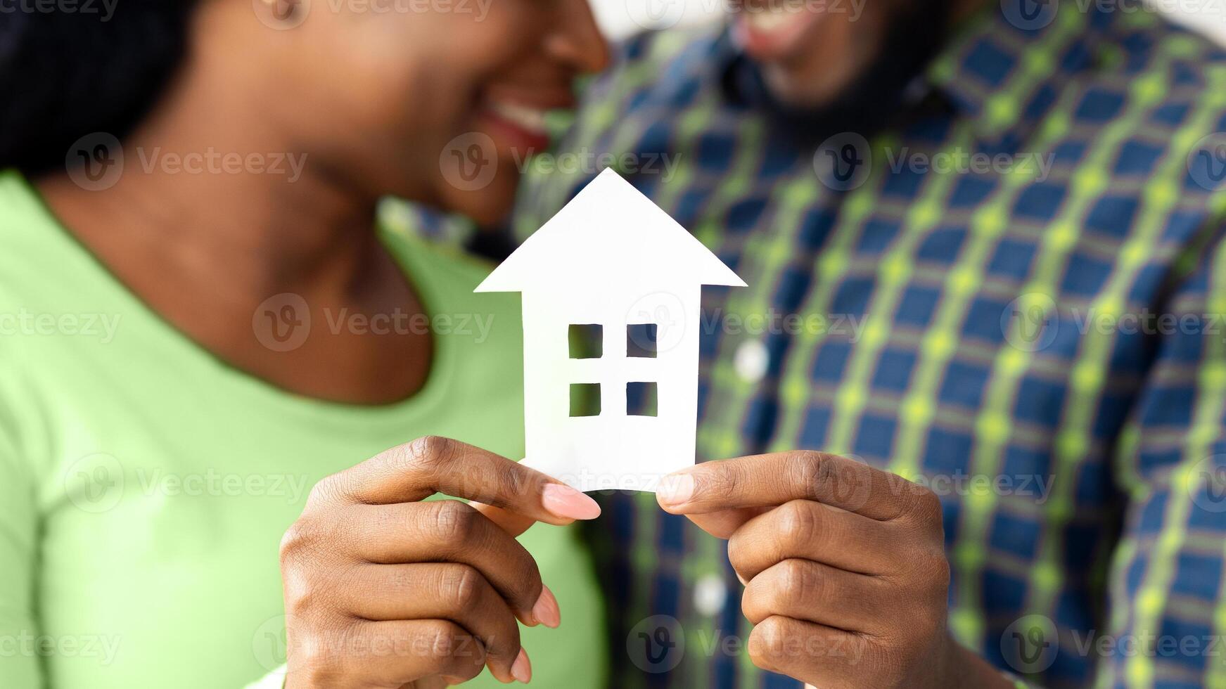 African American Spouses Holding Cutout Paper House Figure In Hands, Celebrating Buying New Property. Conceptual Photo For Family Housing, Real Estate Or Relocation, Closeup With Selective Focus