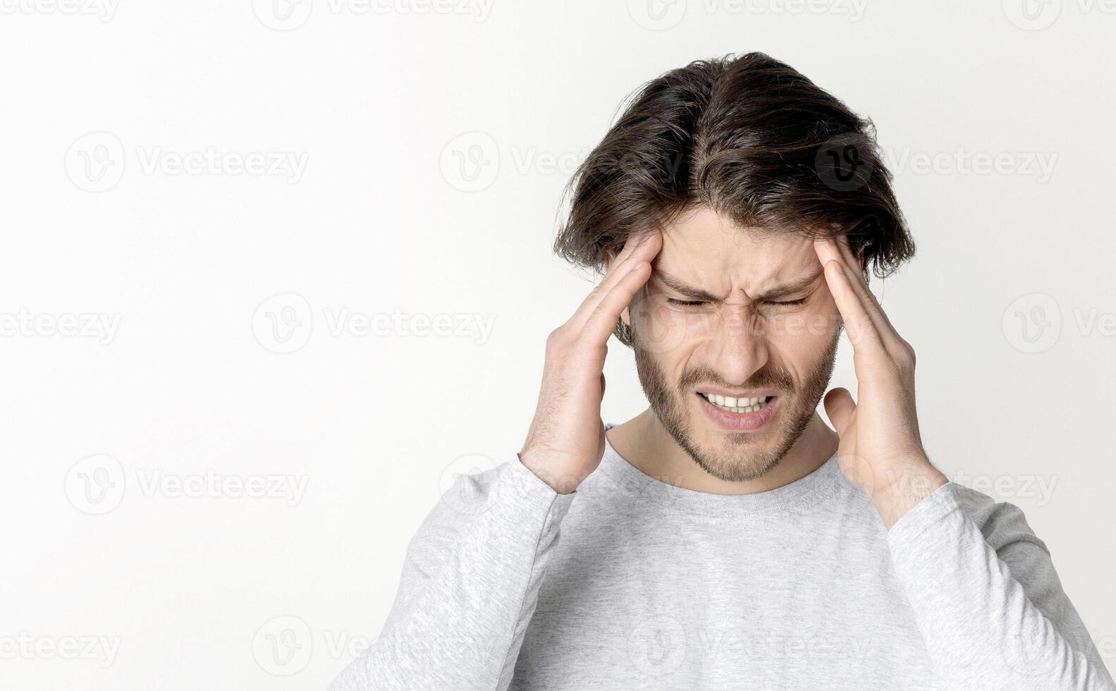 Young man suffering from a headache on gray background. photo