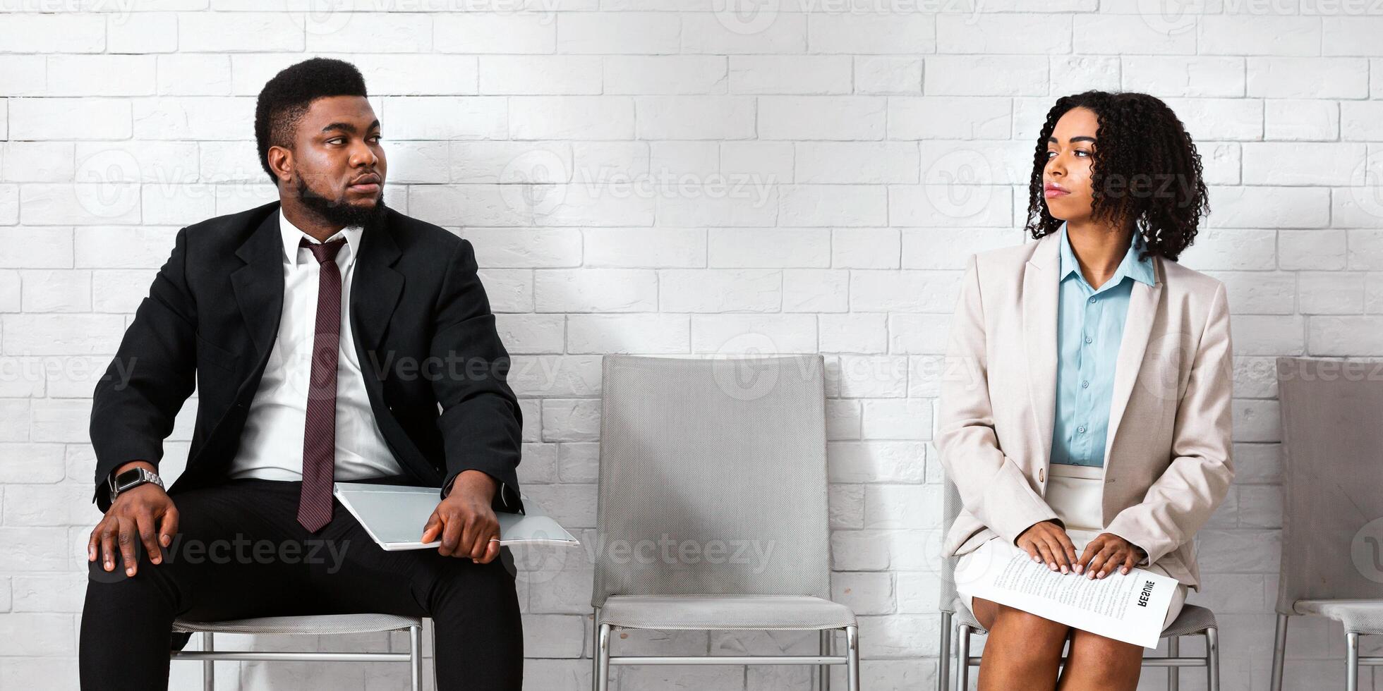 Male and female vacancy candidates looking at each other with antipathy while waiting for job interview in office lobby photo