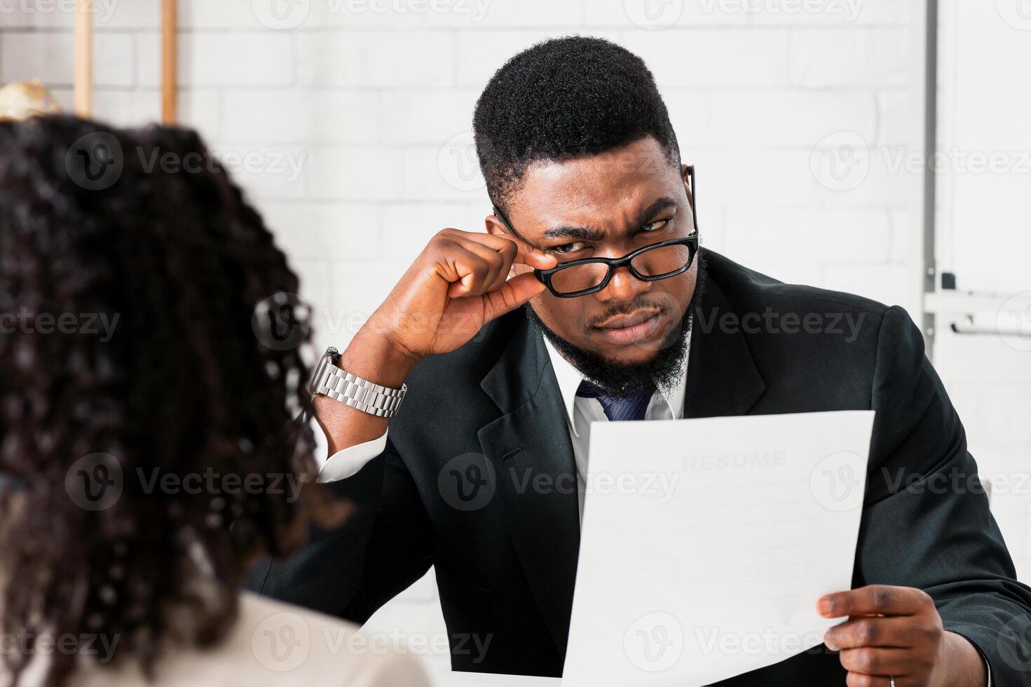 Strict male HR manager reading CV, looking at job applicant with suspicion during employment interview at modern office. Vacancy candidate applying for open position at big company photo