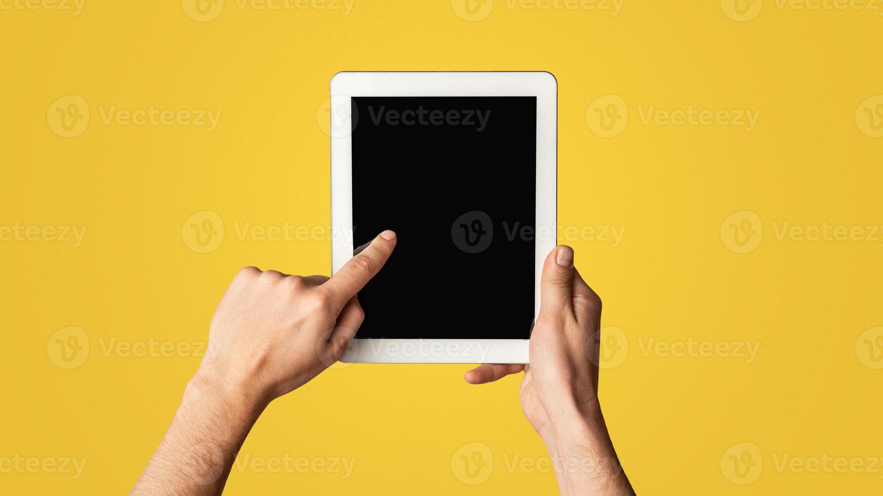 Young man touching blank screen of tablet computer on light background, closeup. Mockup for design. Panorama photo