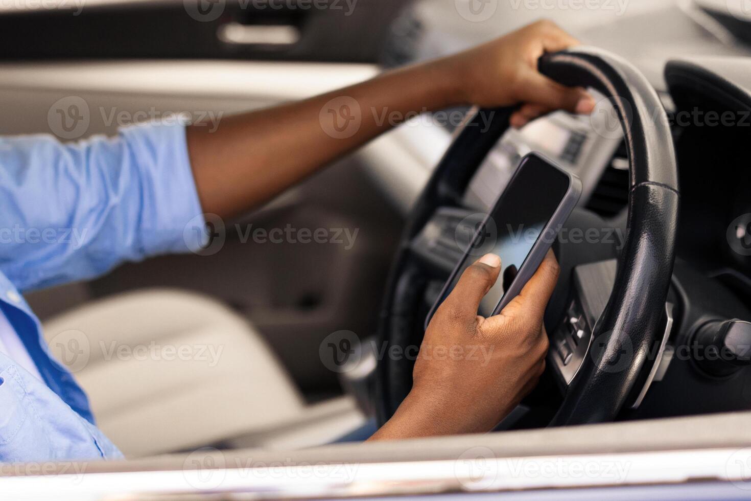 Positive black male driver holding mobile phone while driving nice auto, using new mobile application for navigation going on vacation or making summer trip, stuck in traffic jam, profile side view photo