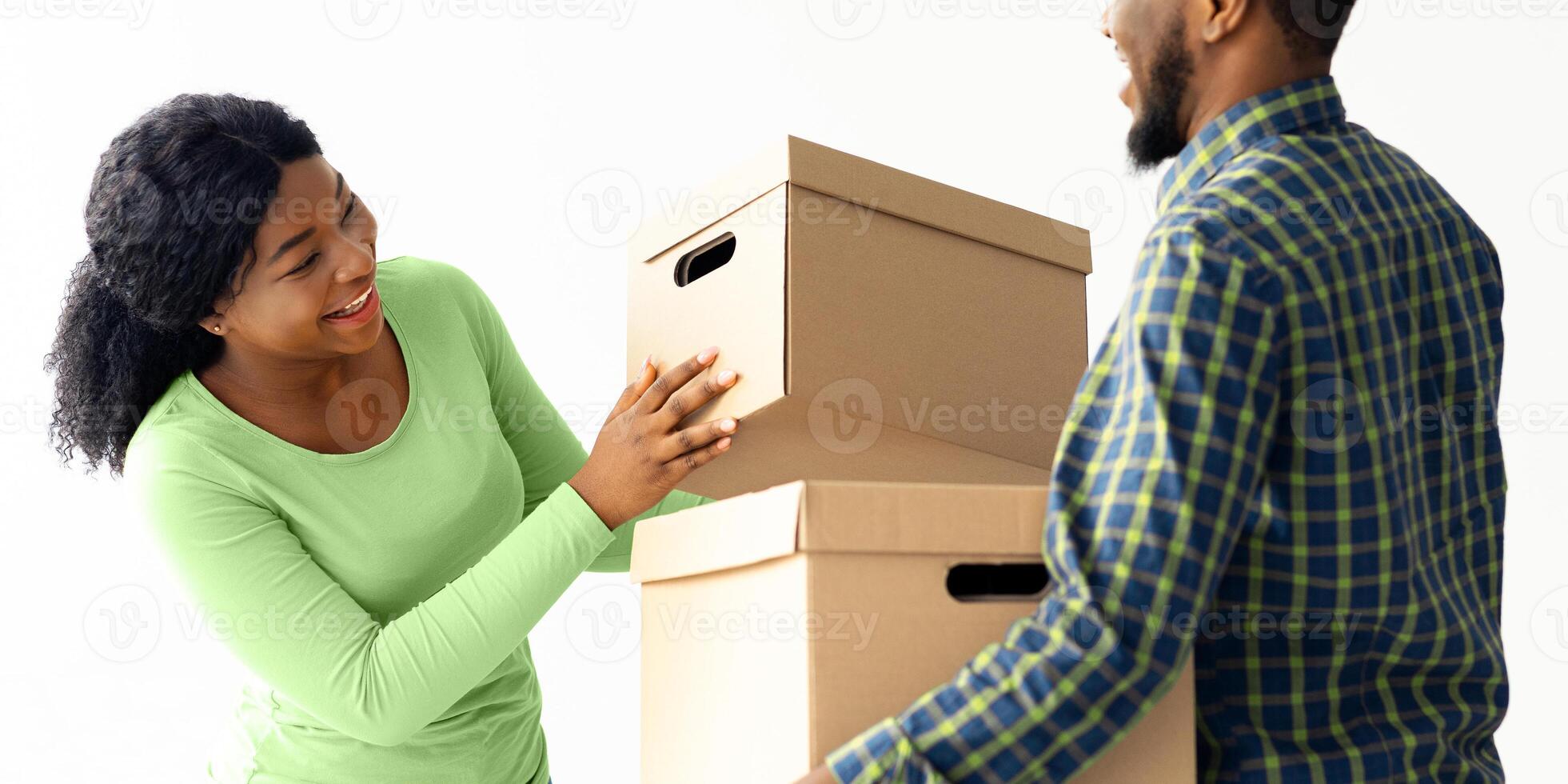 Moving Day. Portrait Of Joyful Young Black Spouses With Cardboard Boxes Packing Belongings During Relocation To New Home, Happy African American Couple Carrying Things And Smiling To Each Other photo