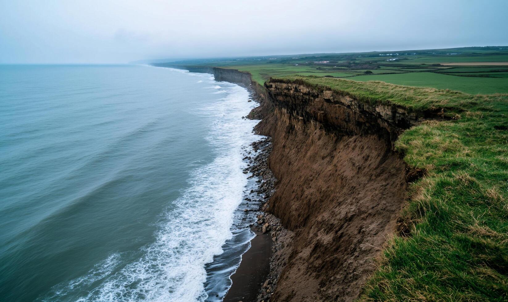 A cliff edge overlooking the ocean and grassy field photo