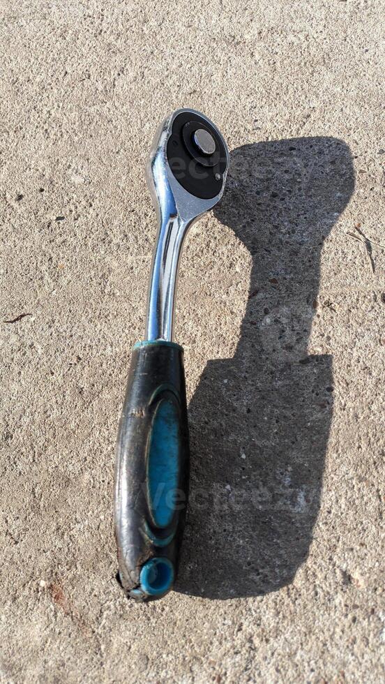 A detailed closeup view of a shiny Chrome Socket Wrench resting on a Concrete Surface photo