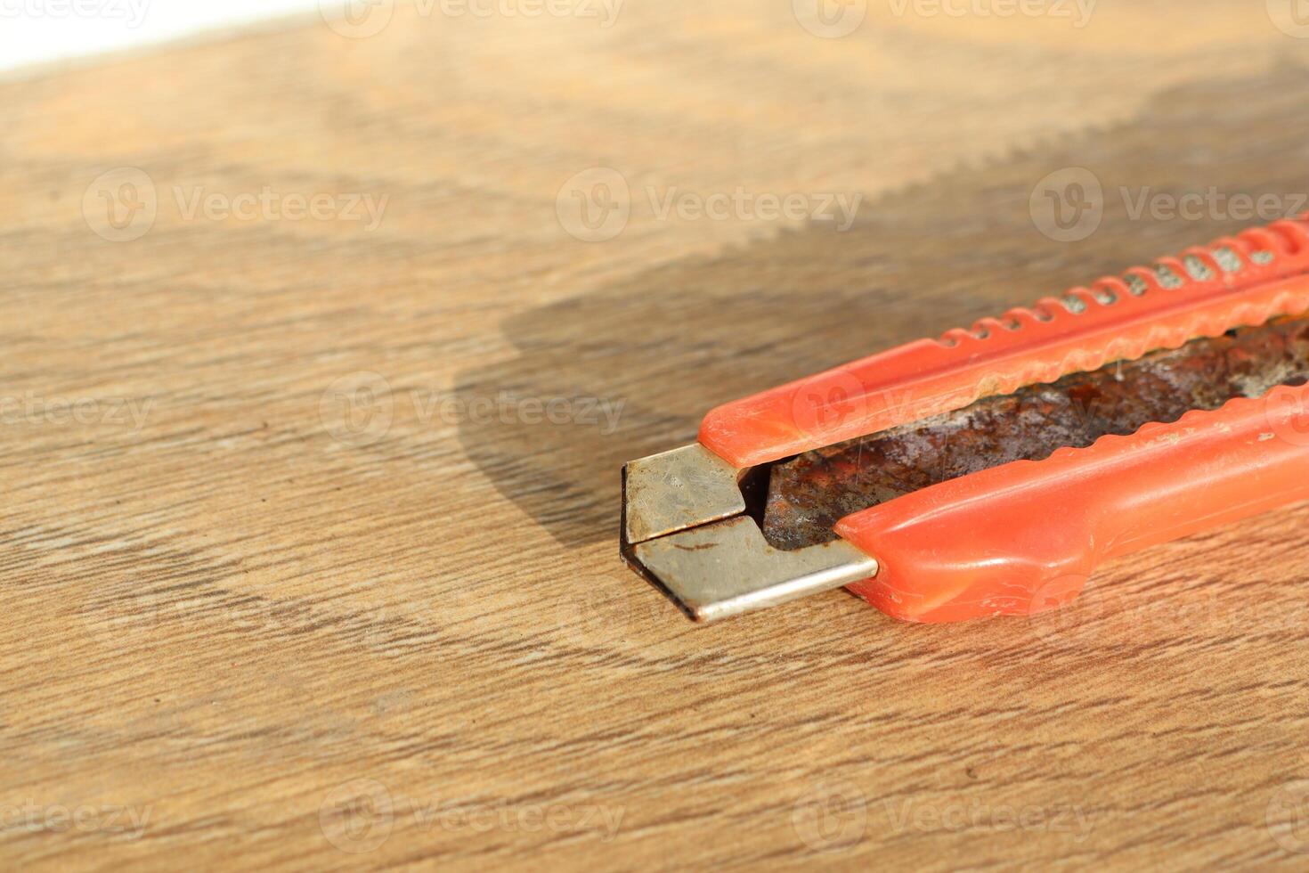 A CloseUp View of a Rusty Utility Knife Resting on a Wooden Surface for Contextual Detail photo