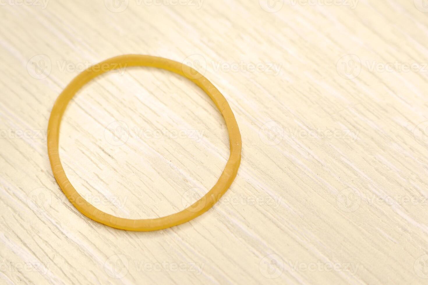 A detailed closeup view of a bright Yellow Rubber Band positioned on a Wooden Surface photo