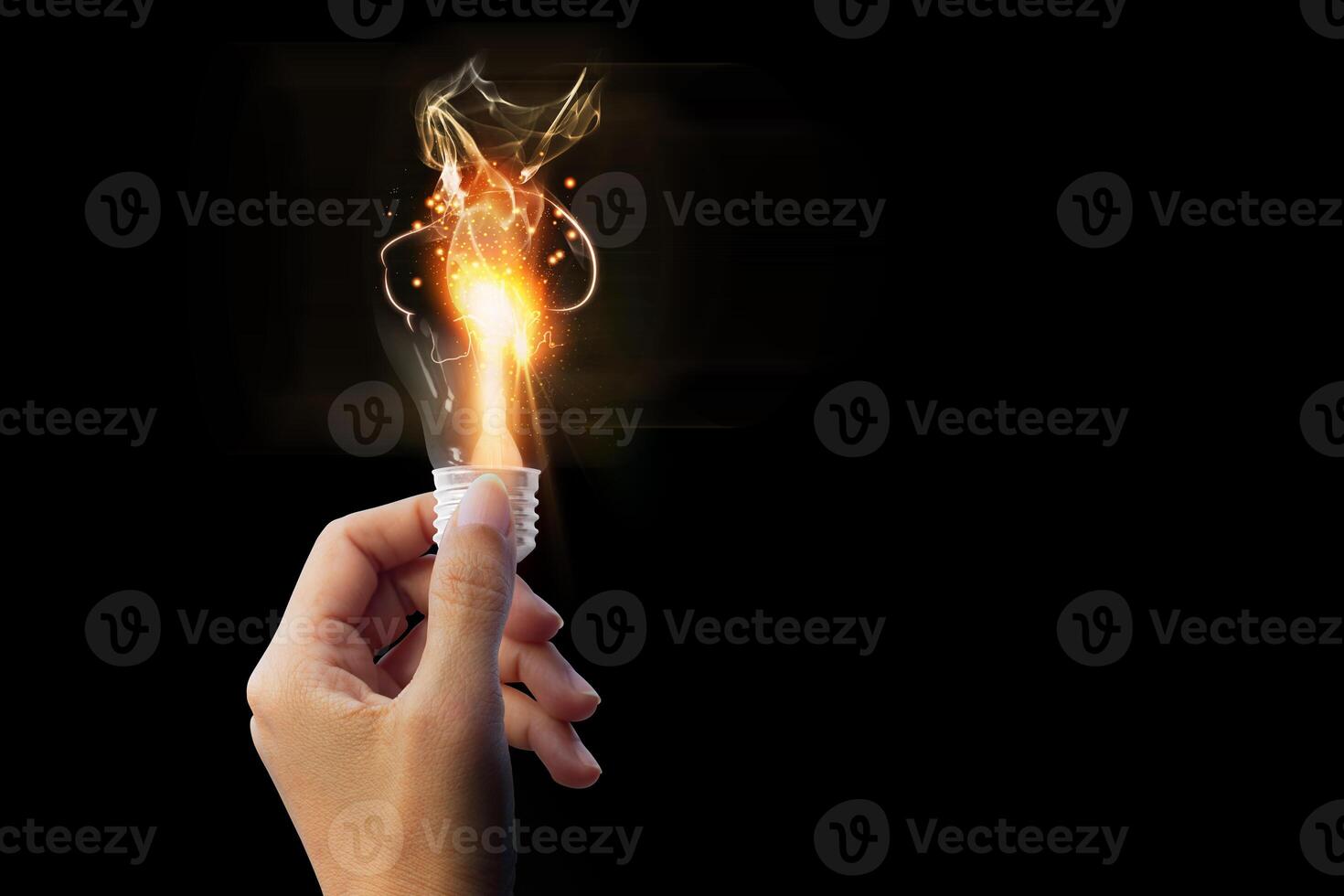 a hand holding a burning light bulb over a black background photo