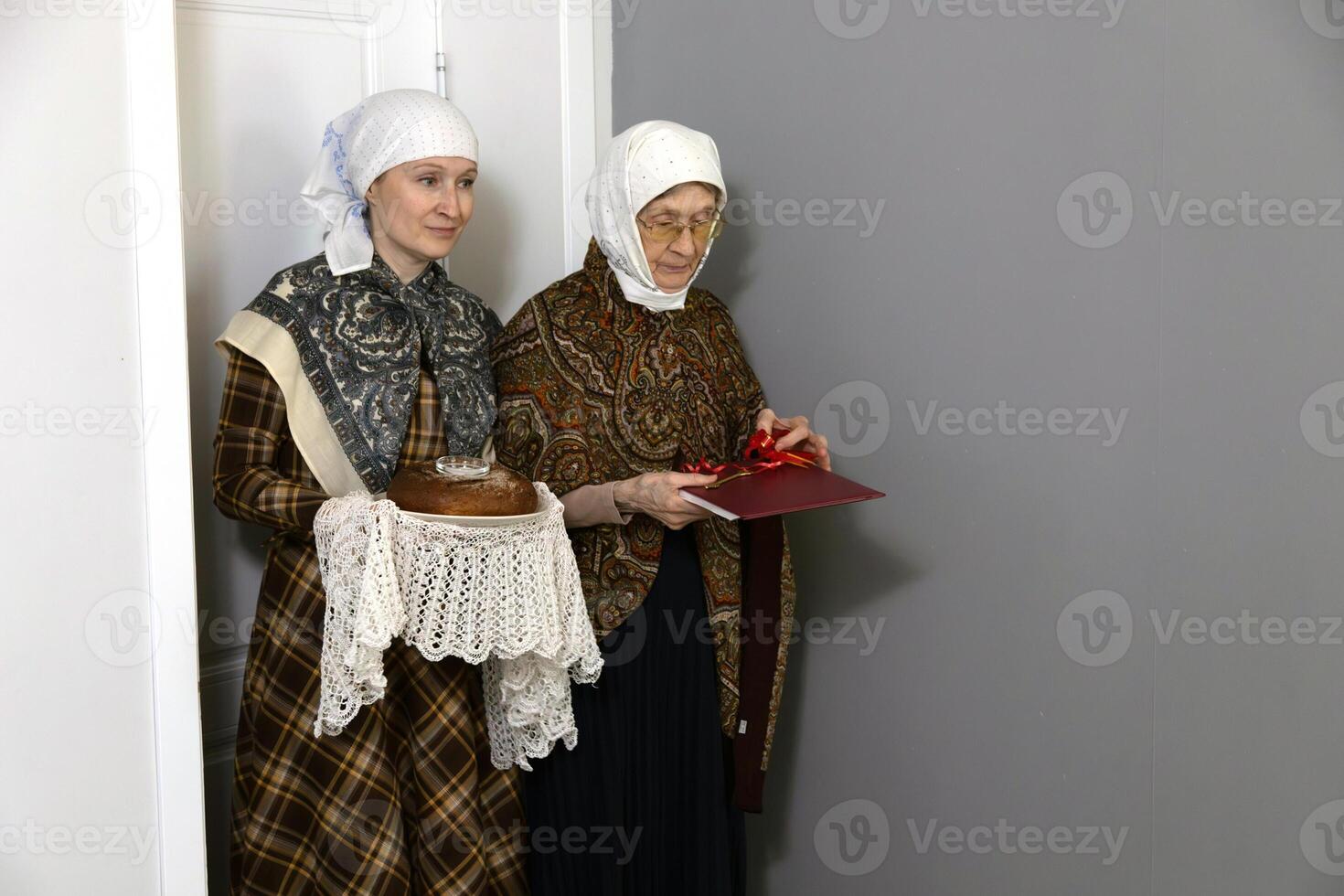 Housewarming, an elderly woman and adult woman carry bread and salt, documents and the key to a new house. Real estate, rent, mortgage, space for text. photo