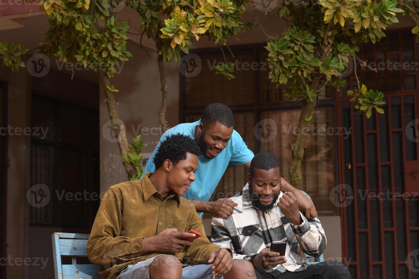 three students standing together in a school courtyard. They are engaged with their smart phones, absorbed in their devices. photo